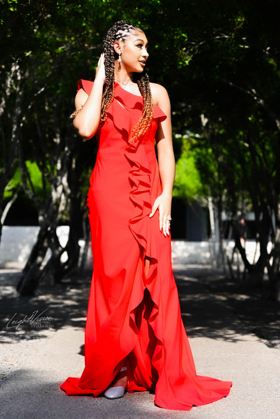 A woman in a striking red dress poses for a photo, exuding charm and sophistication.
