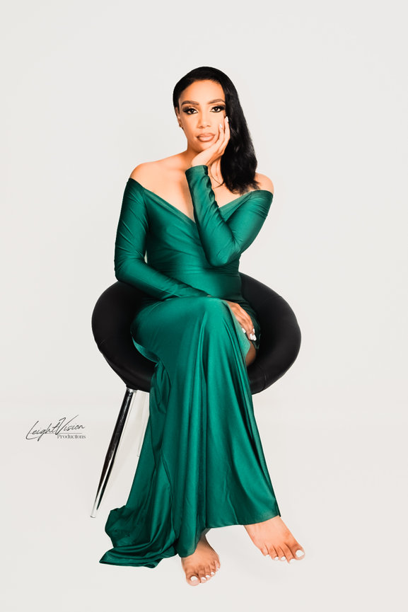 A woman in a green dress is comfortably seated on a chair, reflecting a sense of calm and sophistication.