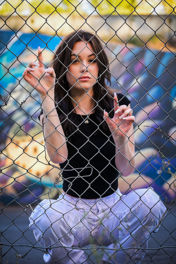 Senior year photo of girl behind a fence with graffiti in background. Eagle, Idaho