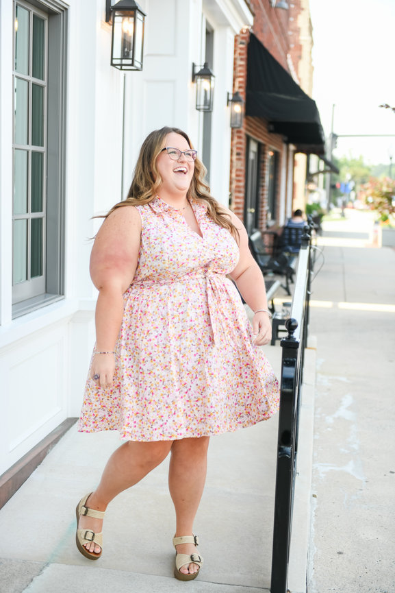Smiling woman in floral dress walking on sidewalk in downtown Mocksville, NC during a branding session.