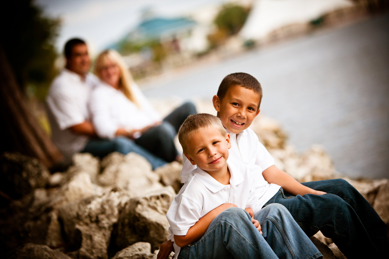 Family sitting on rocks by a river with two children in the foreground
