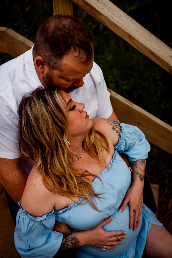 Couple lovingly embraces on wooden steps; the woman in a blue dress, the man in a white shirt.