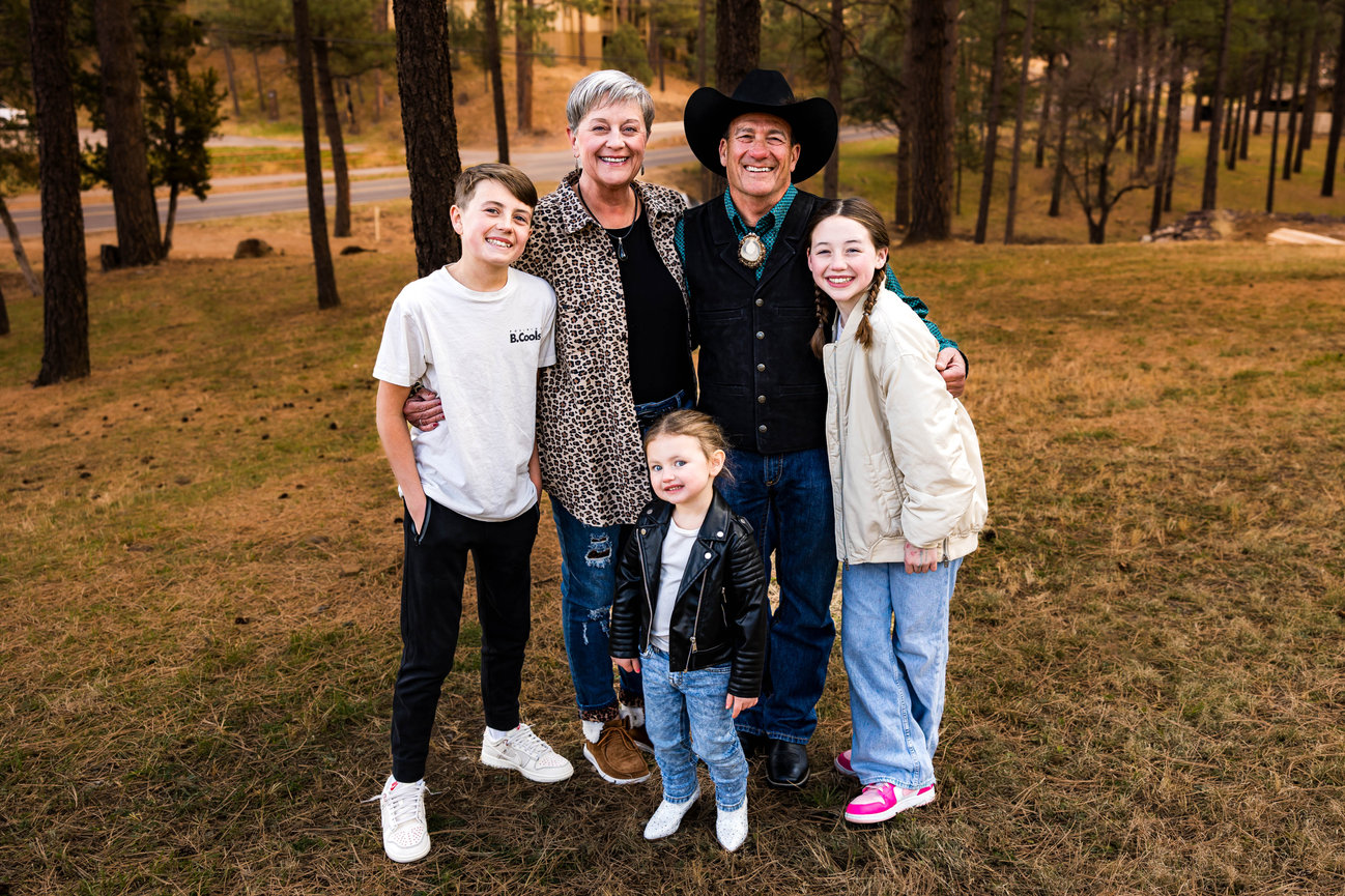 Grandparents with three grandchildren posing for an outdoor family portrait in Ruidoso, NM, surrounded by trees in a forested area.