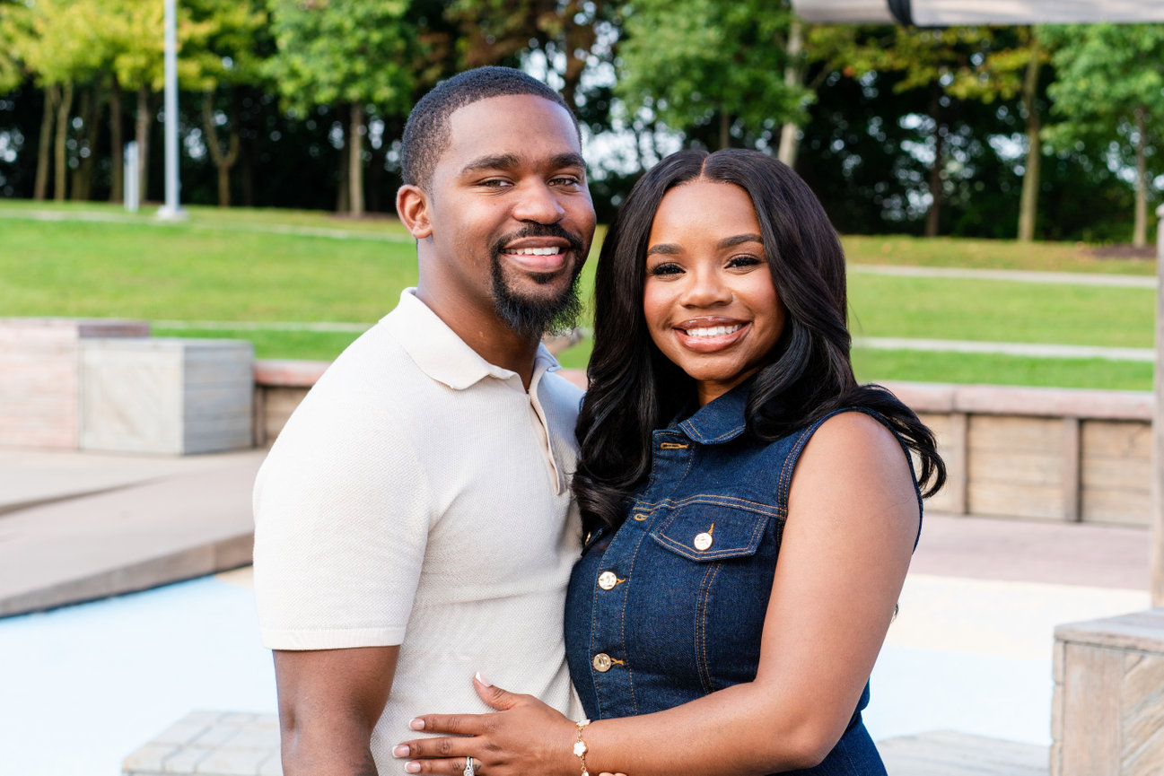 Smiling couple posing outdoors in a park, with the woman embracing the man
