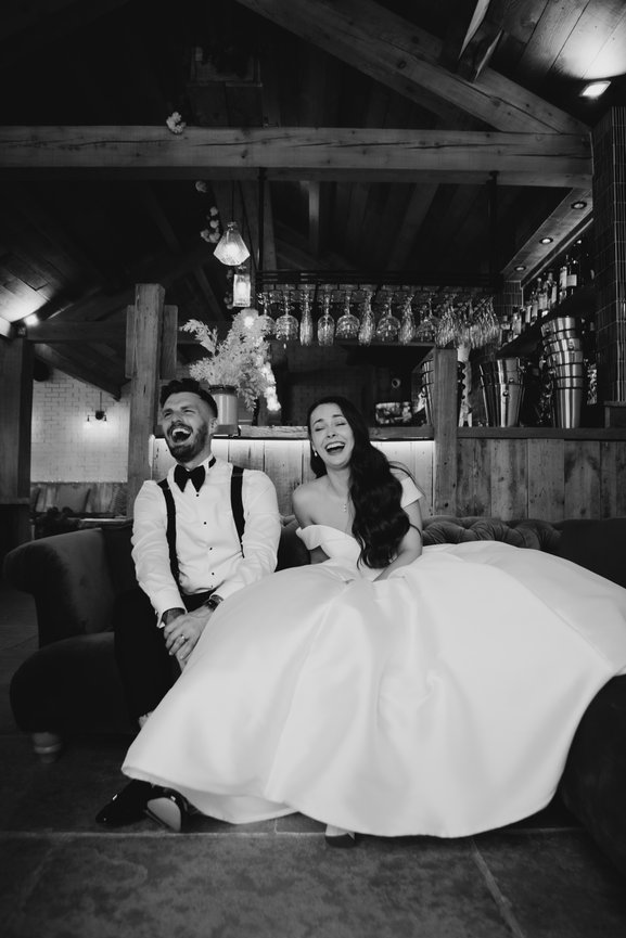 B&W Editorial wedding photography at Eden Barn: A couple in black tie laughing on a couch.
