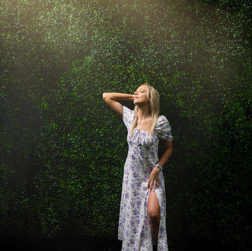 Woman in a floral dress standing by a wall of greenery