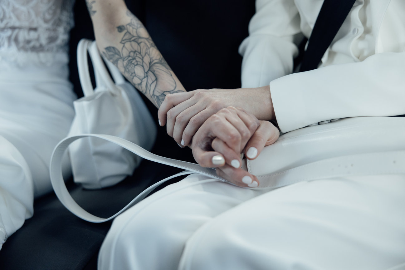 Modern editorial bridal portrait: Two brides holding hands, with a sleek bridal clutch bag.
