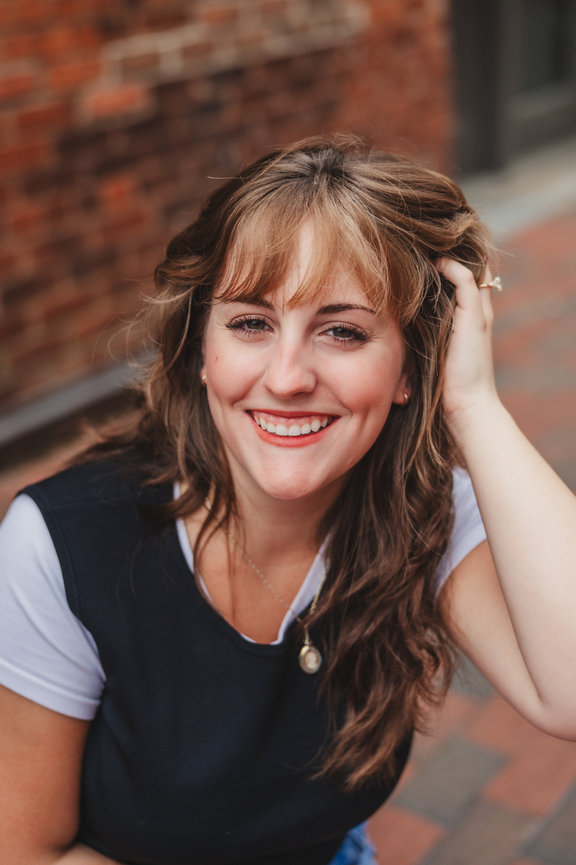 Close-up portrait of a smiling woman with bangs and hand in her hair.