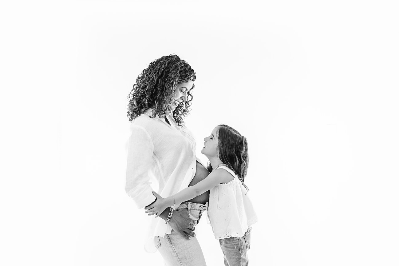 Editorial family maternity portrait of pregnant mom and young daughter in black and white white studio with soft window light