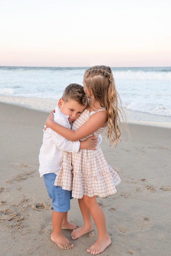 Big sister hugging little brother during golden hour on the beach