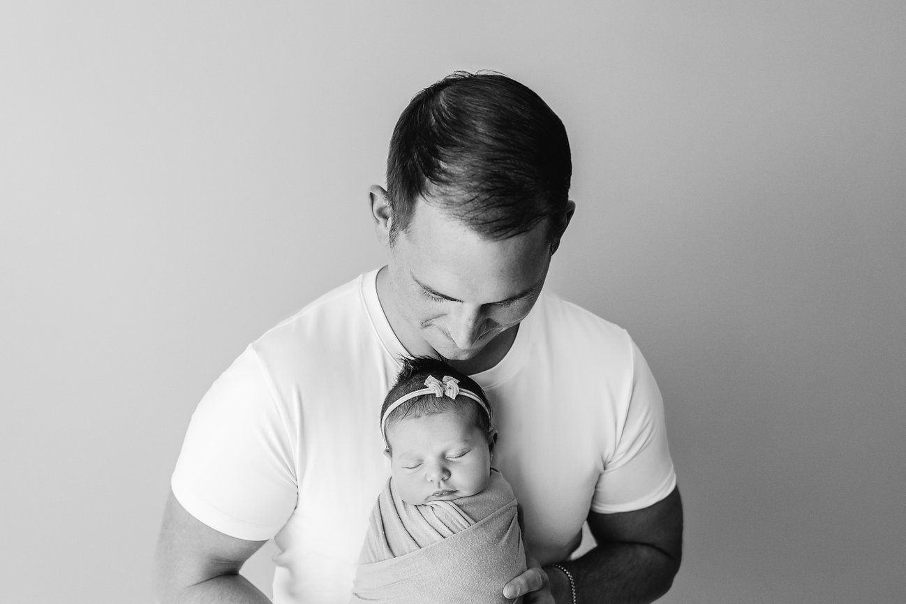 Dad holding swaddled newborn gently in hands, captured with natural connection and strength