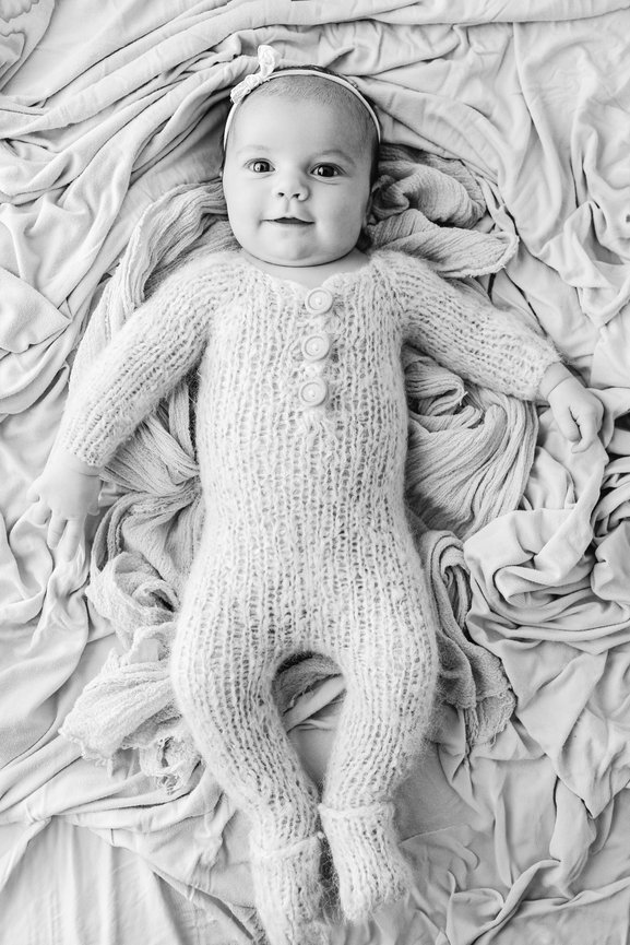 Full-body lifestyle shot of newborn awake and alert on white surface in light-filled Manasquan studio