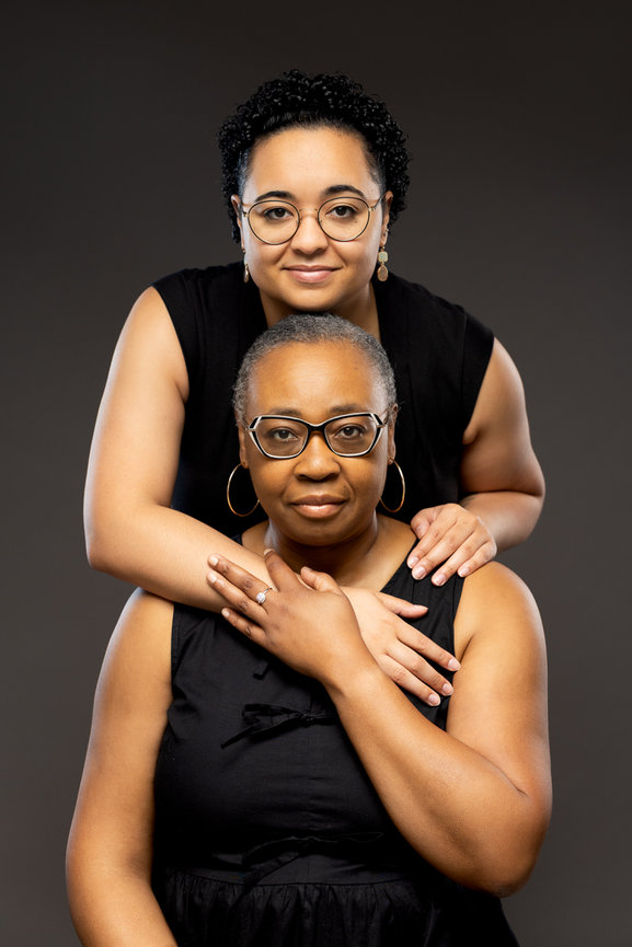Mom and Daughter pose in studio portrait embracing wearing simple black on dark backdrop