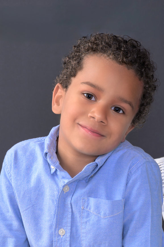 young boy tilting his head wearing a blue button down shirt having his headshot done for a casting call
