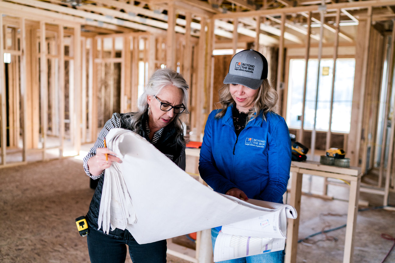Two people studying a floor plan inside a framed house under construction