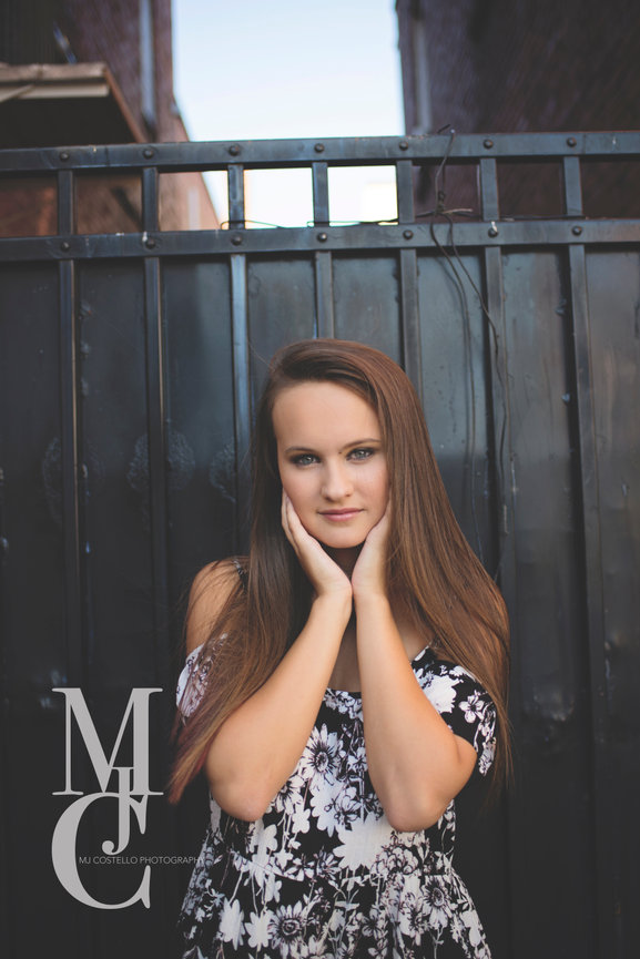 Teen girl posing with hands on her face in front of a dark fence