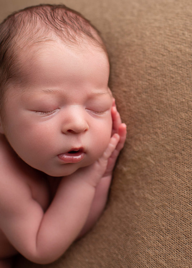 Close up newborn photo of baby boy sleeping peacefully with praying hands under his cheek during newborn photography session with Kansas City newborn photography Dreamworks Photography 