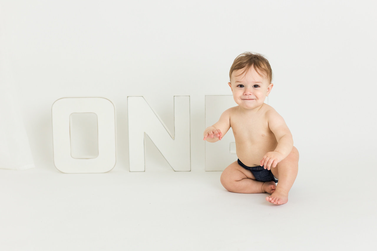 A baby crawling in front of the word one, symbolizing early milestones in development during his cake smash photo session with Catherine Whitney Photography
