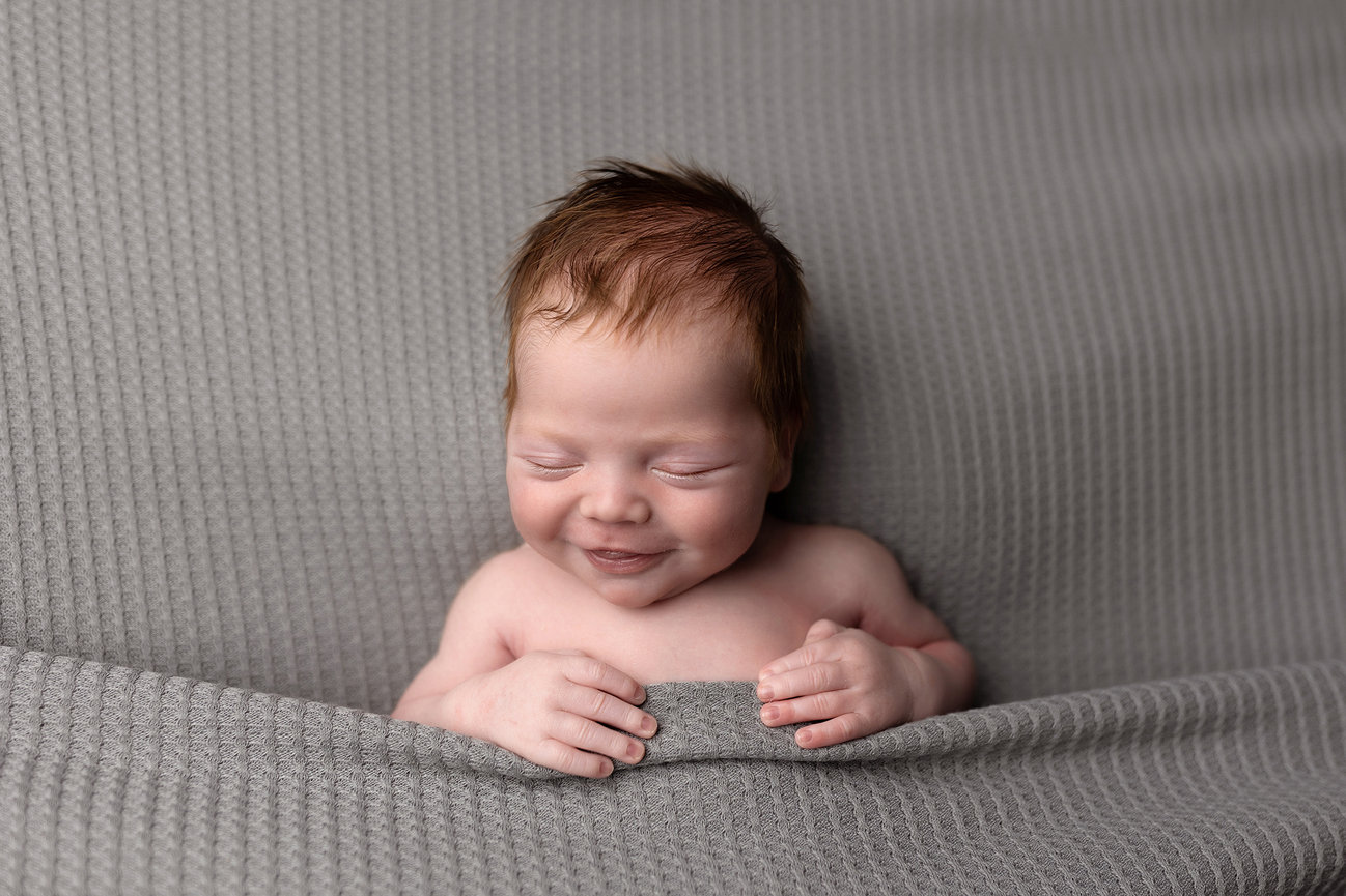 Smiling baby wrapped in a textured gray blanket photo taken by Omaha Photographer