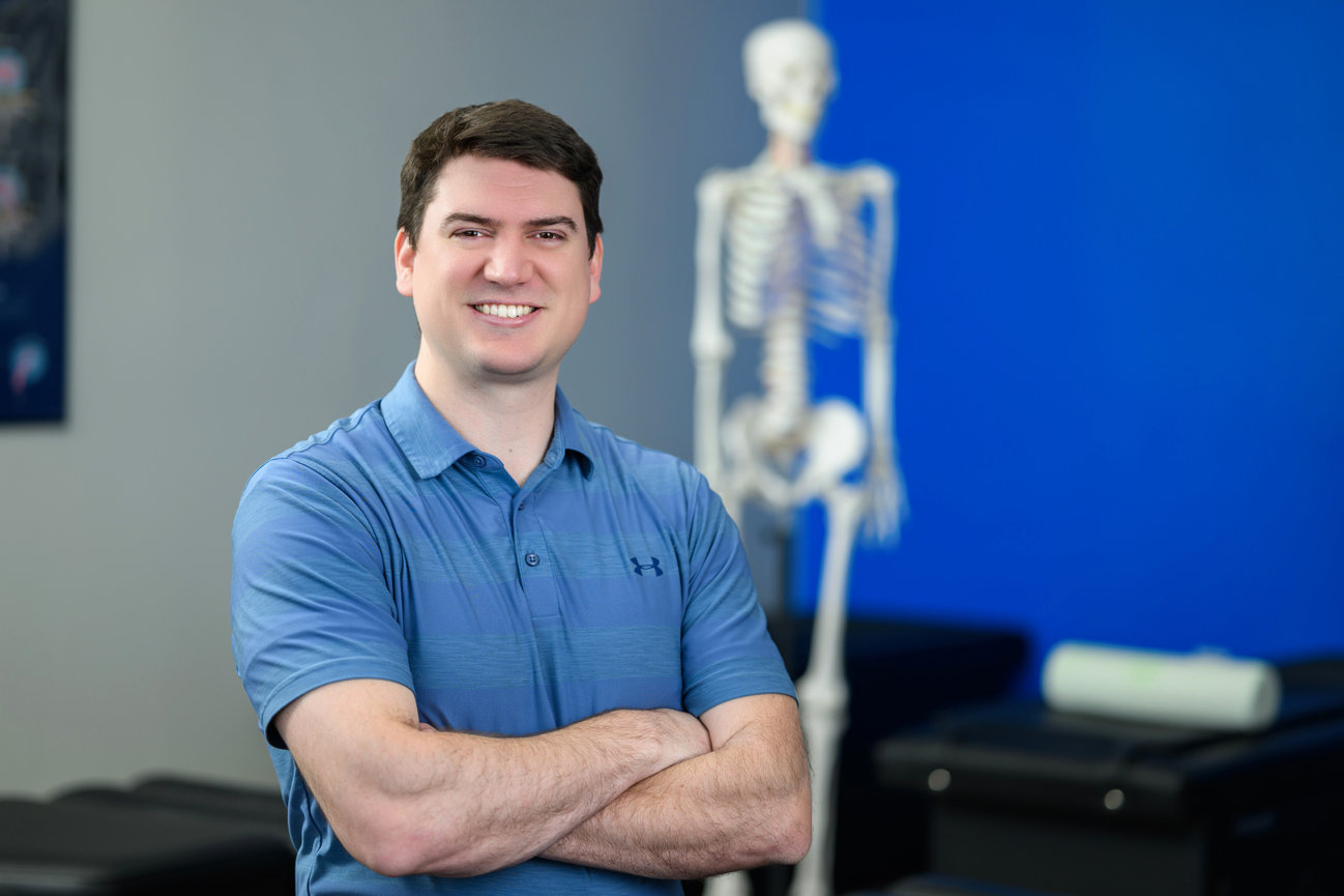 A male chiropractor with his arms folded smiling at the camera.