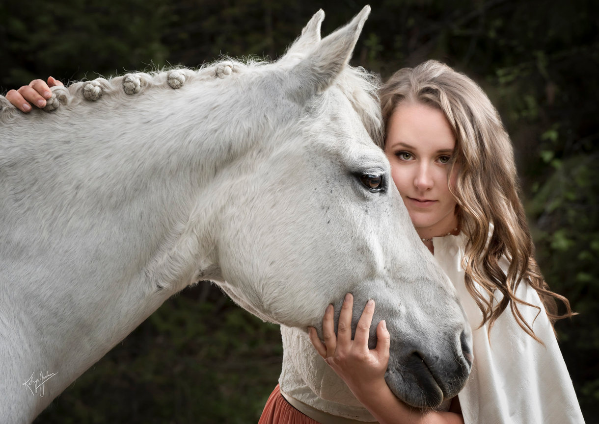 Close up portrait of a woman embracing the head of a white horse that we see in profile.