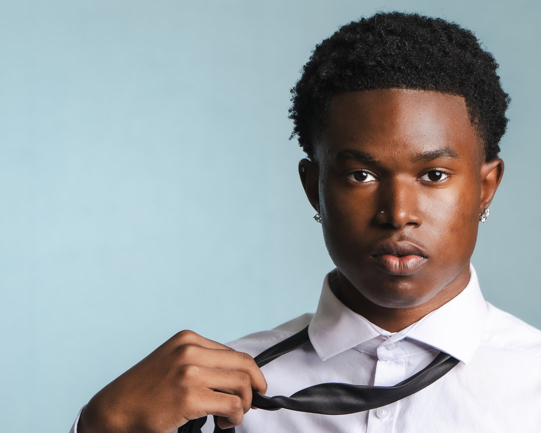 Portrait of a young person in a white shirt adjusting a black tie against a light blue background