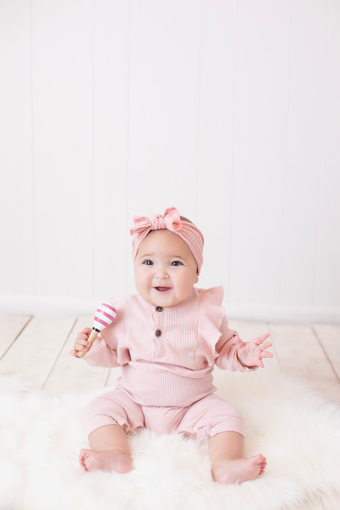 Baby sitting in pink with a matching bow against a soft cream set