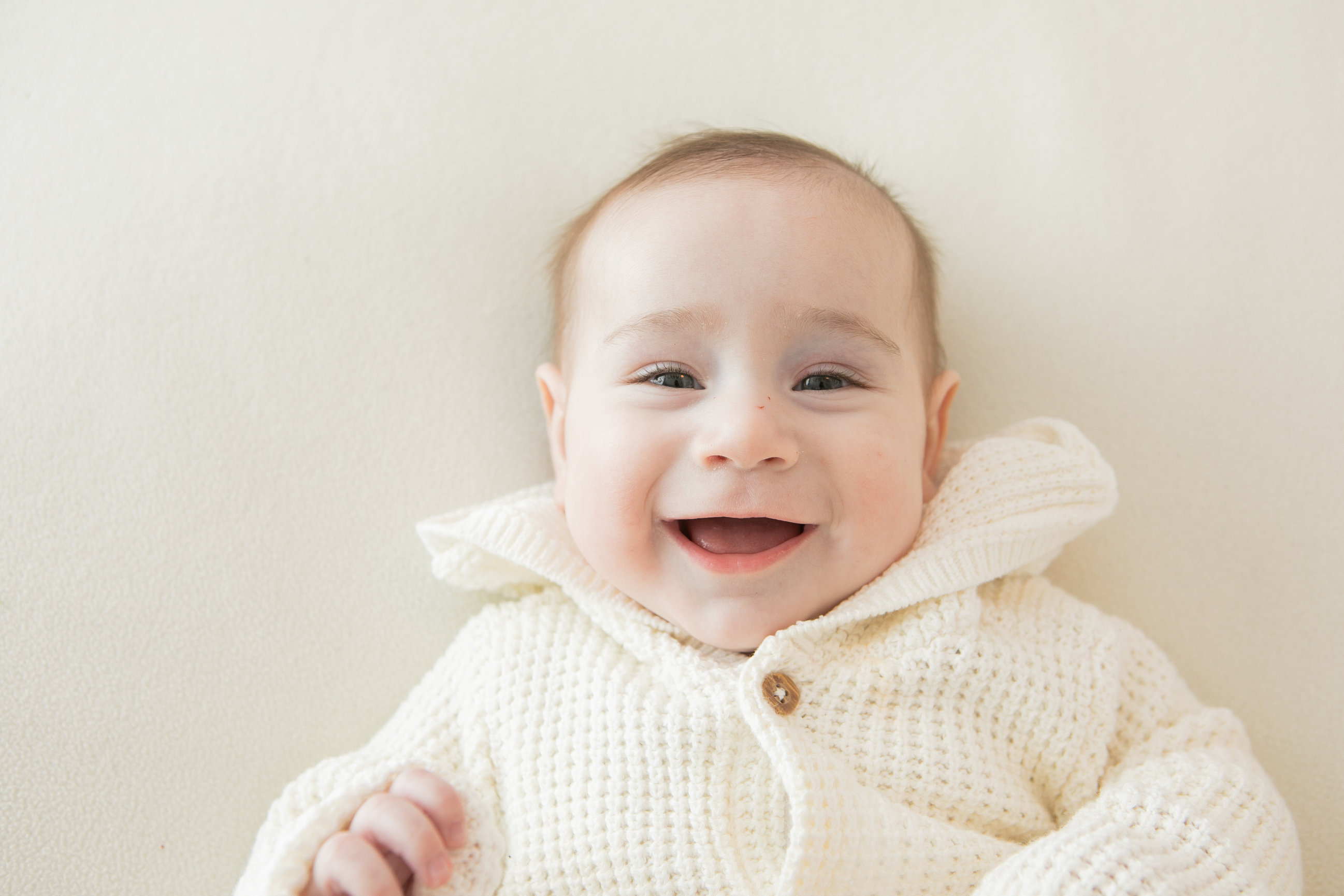Baby laughing in a cream knitted jumper