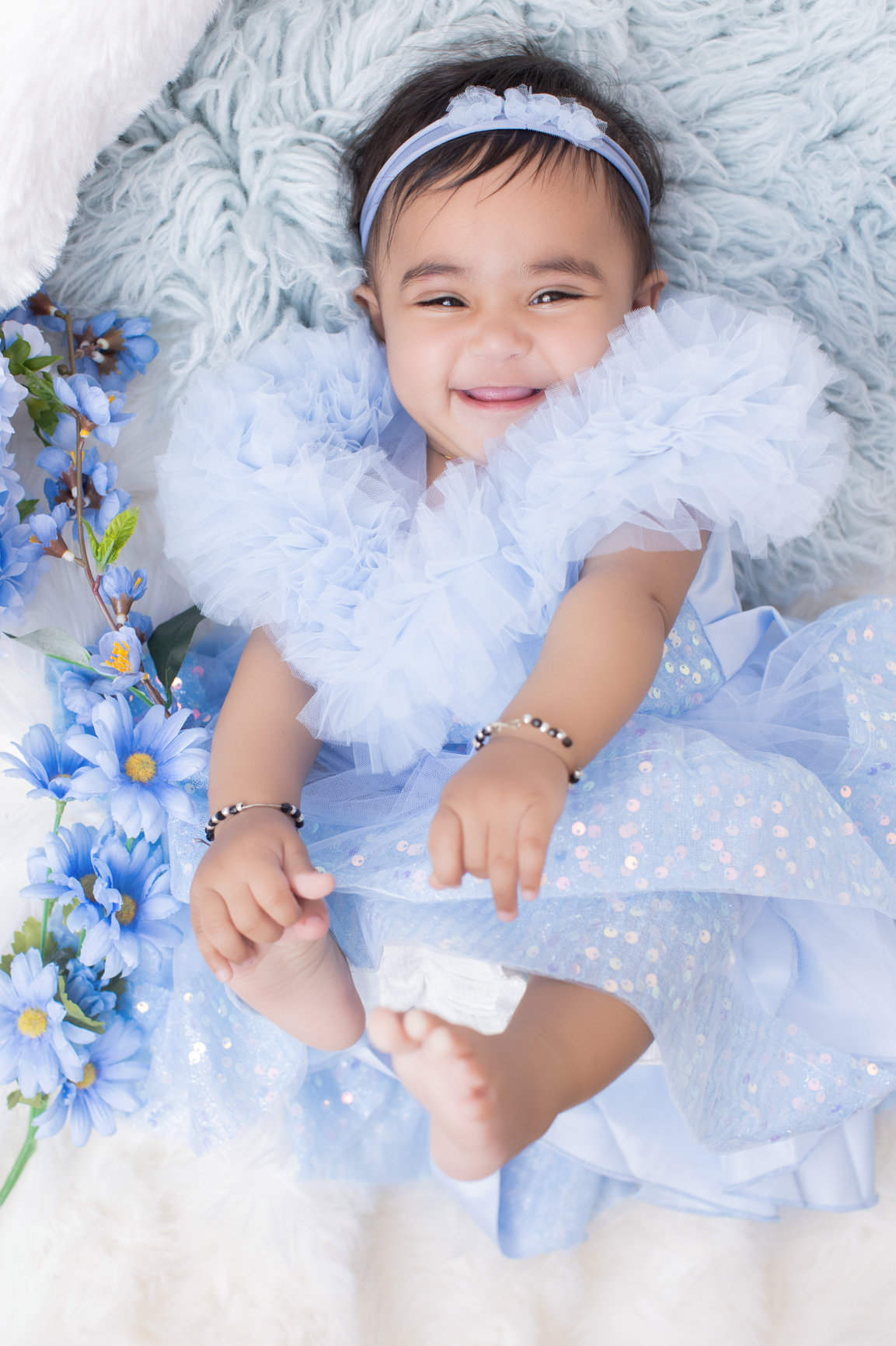 Baby in pale blue tulle lying among blue flowers