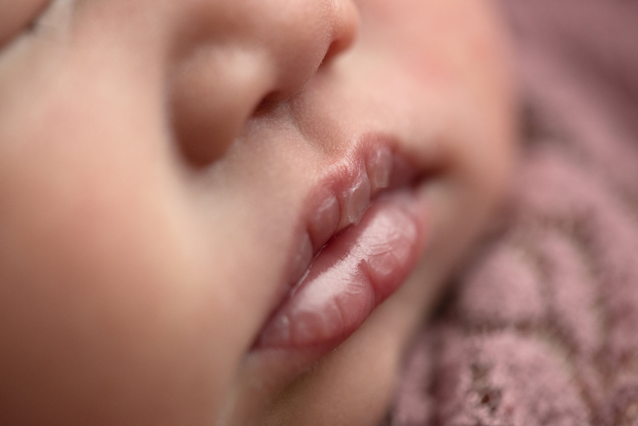 Close-up of a babys face, lips slightly open, showing soft, delicate skin. The baby rests against a textured pink blanket in Hanover Park, creating a warm and peaceful atmosphere.