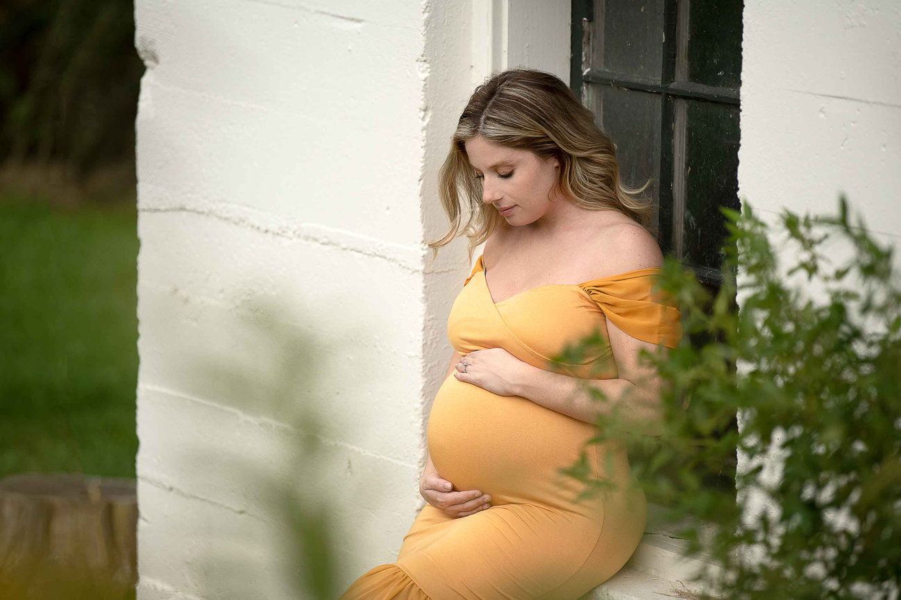 new mother sitting on a ledge wearing a yellow dress