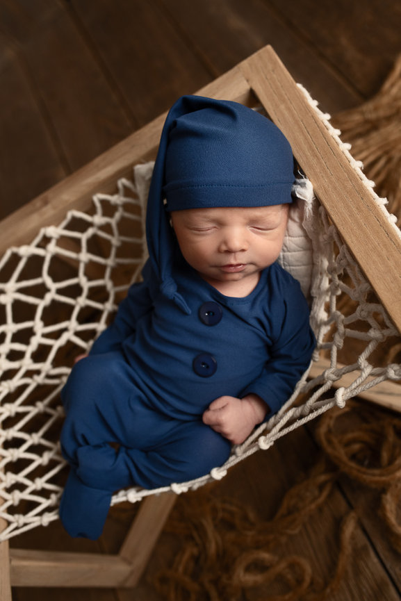 Newborn baby boy in a cozy blue sleeper and nightcap, peacefully sleeping in a macrame hammock – newborn photography session in Algonquin, Illinois