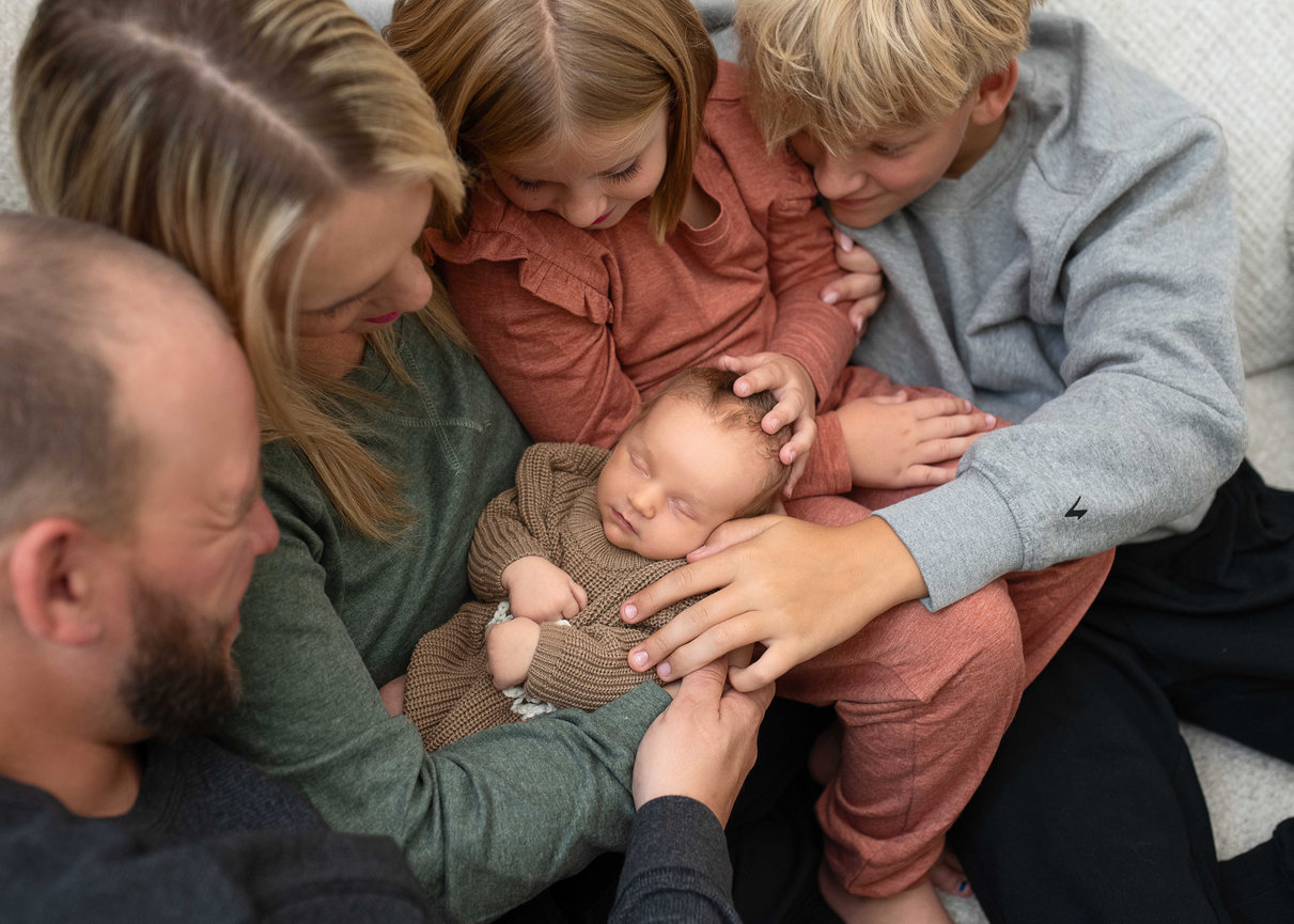 Family gathered around a sleeping newborn, sharing a tender moment on a cozy couch.