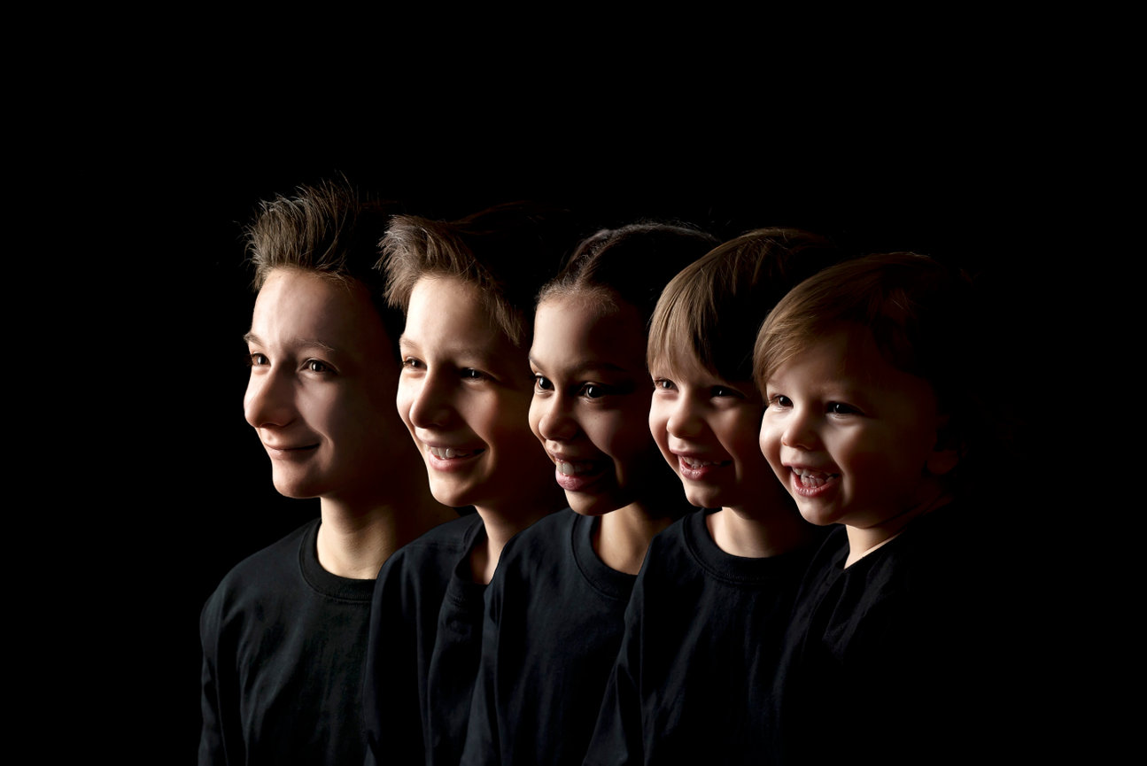 Five children in black shirts smiling against a dark background.