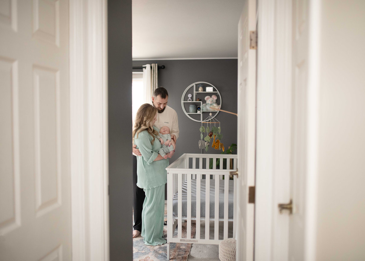 Parents holding a baby in a nursery beside a white crib