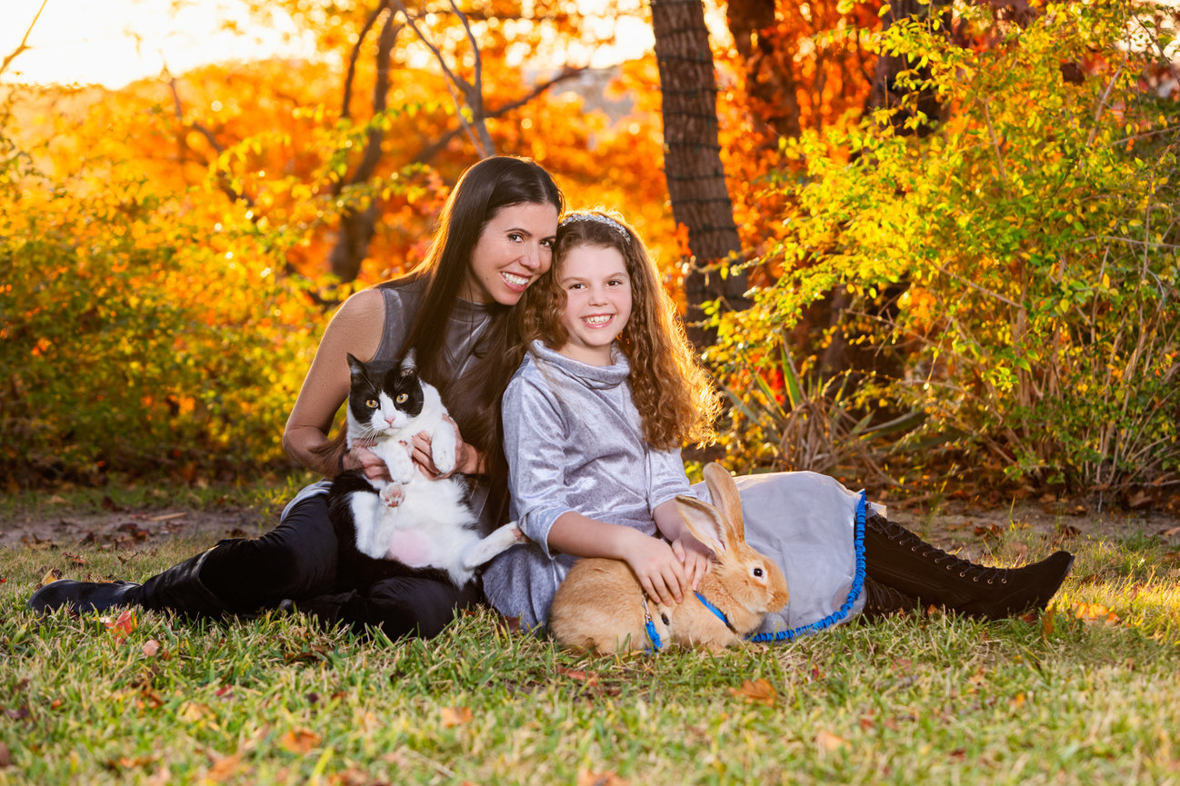 Outdoor portrait of mom, daughter, cat and a rabbit at sunset.