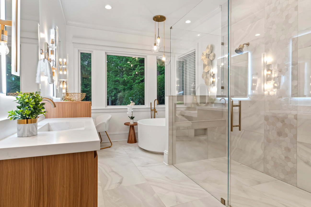 Luxury modern bathroom with glass shower, freestanding tub, double vanity, and large windows overlooking trees