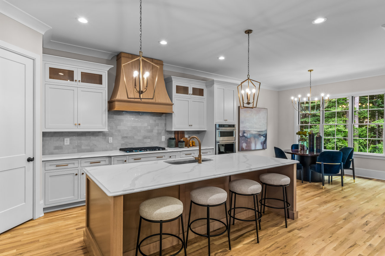 Bright modern kitchen with white cabinets, island seating, gold pendant lights, and dining nook by large windows