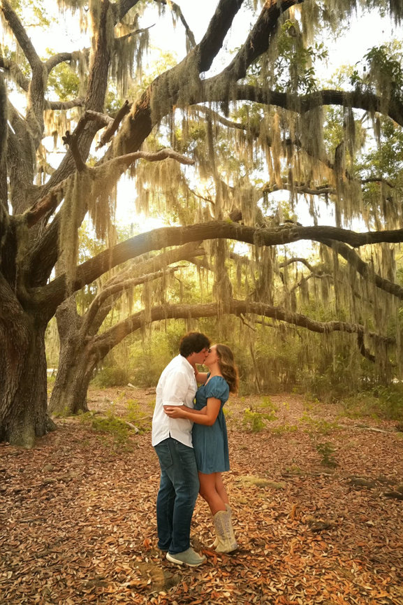 Couple kissing beneath hanging moss in a wooded park.