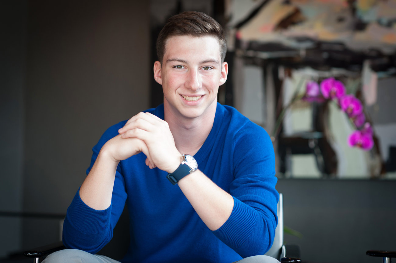 Dark haired teenage boy in a bright blue long sleeved shirt sitting in a chair for his senior pictures in Dublin OH.