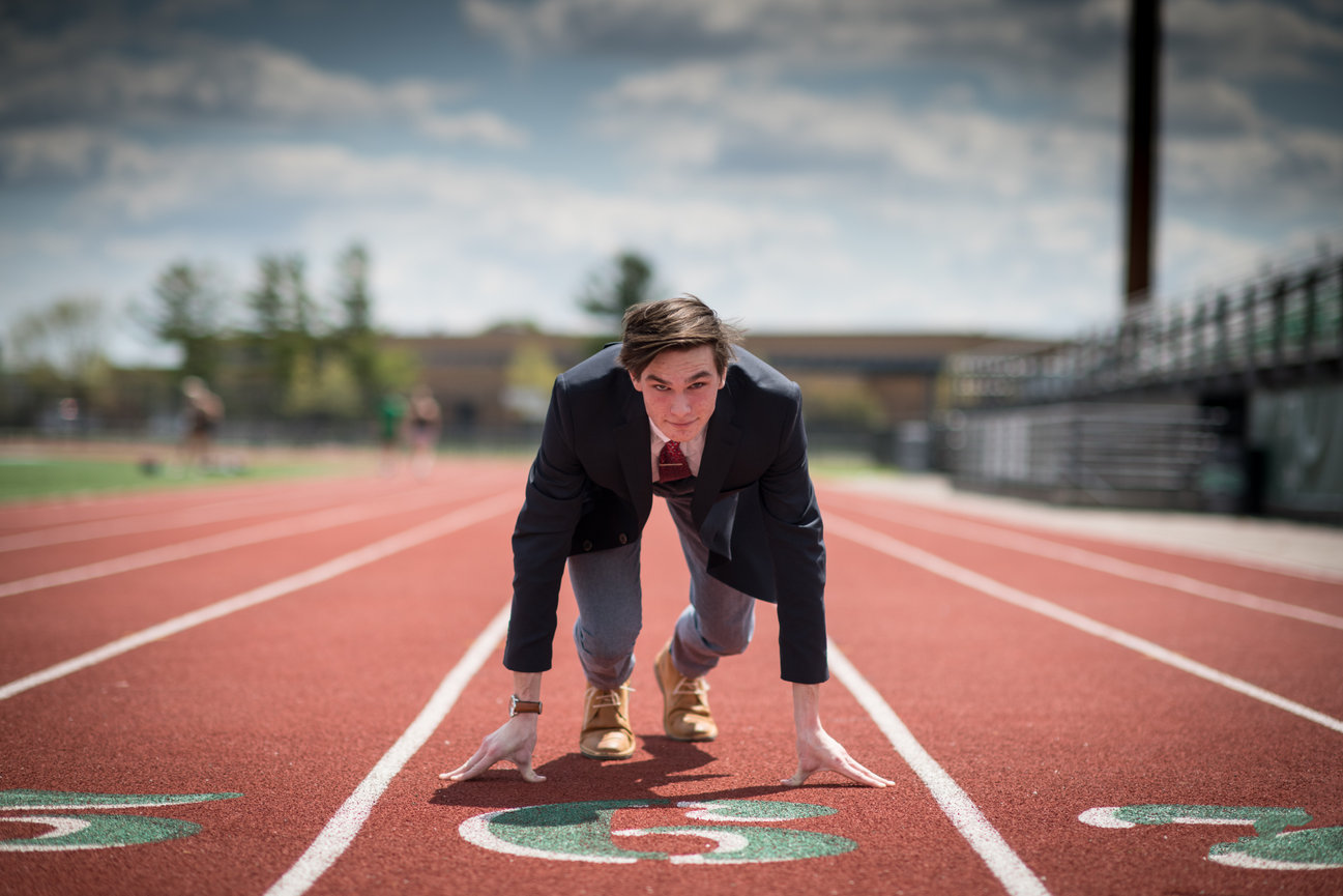 Man in a suit crouched at the beginning of a track race, preparing to sprint.