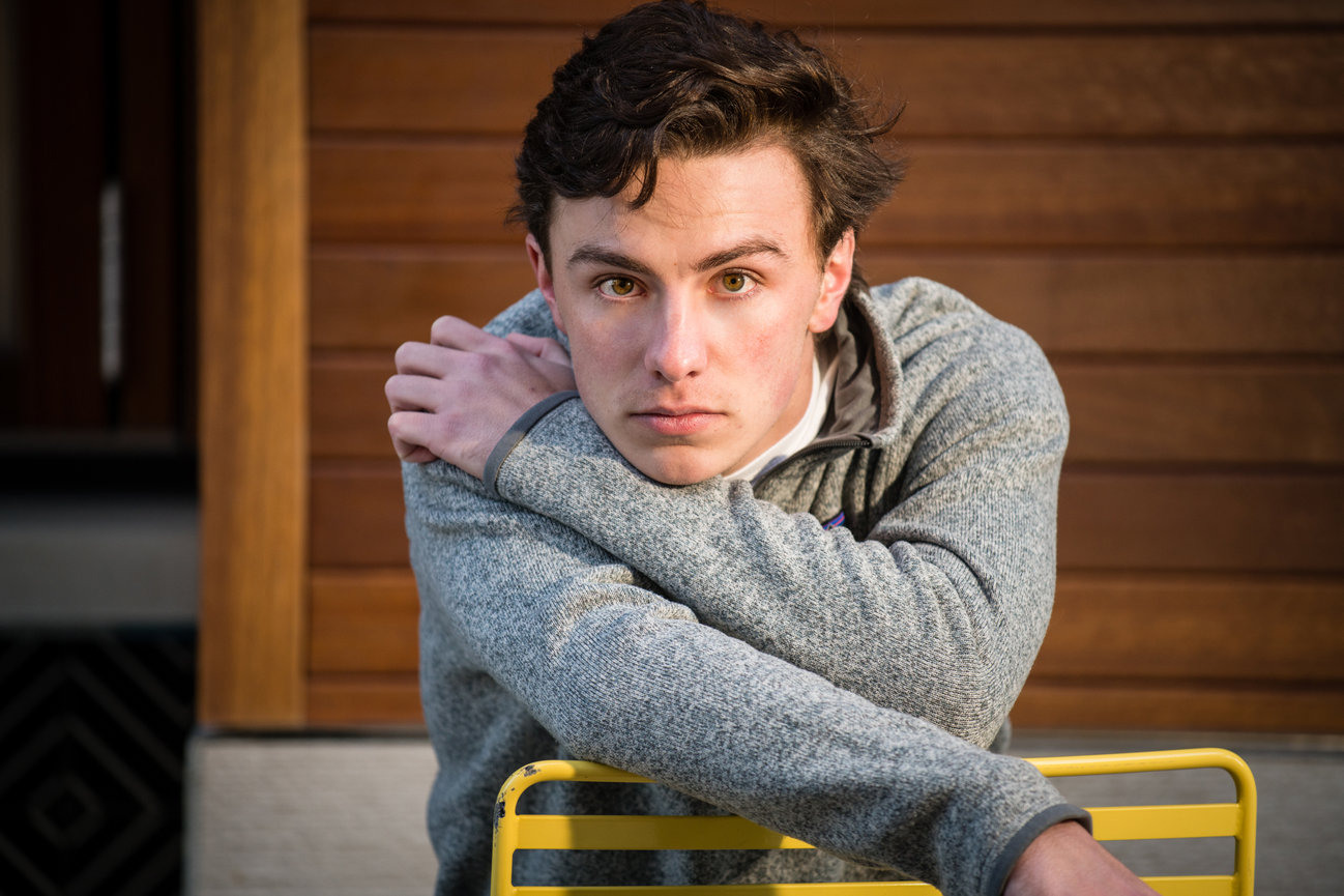 Dark haired teenage boy posing on a yellow metal chair for senior pictures in Dublin OH.