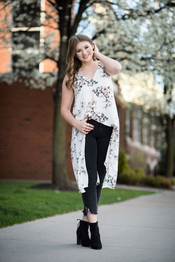 Teenage girl in a floral blouse and black jeans posing outdoors for her senior pictures in Dublin OH.