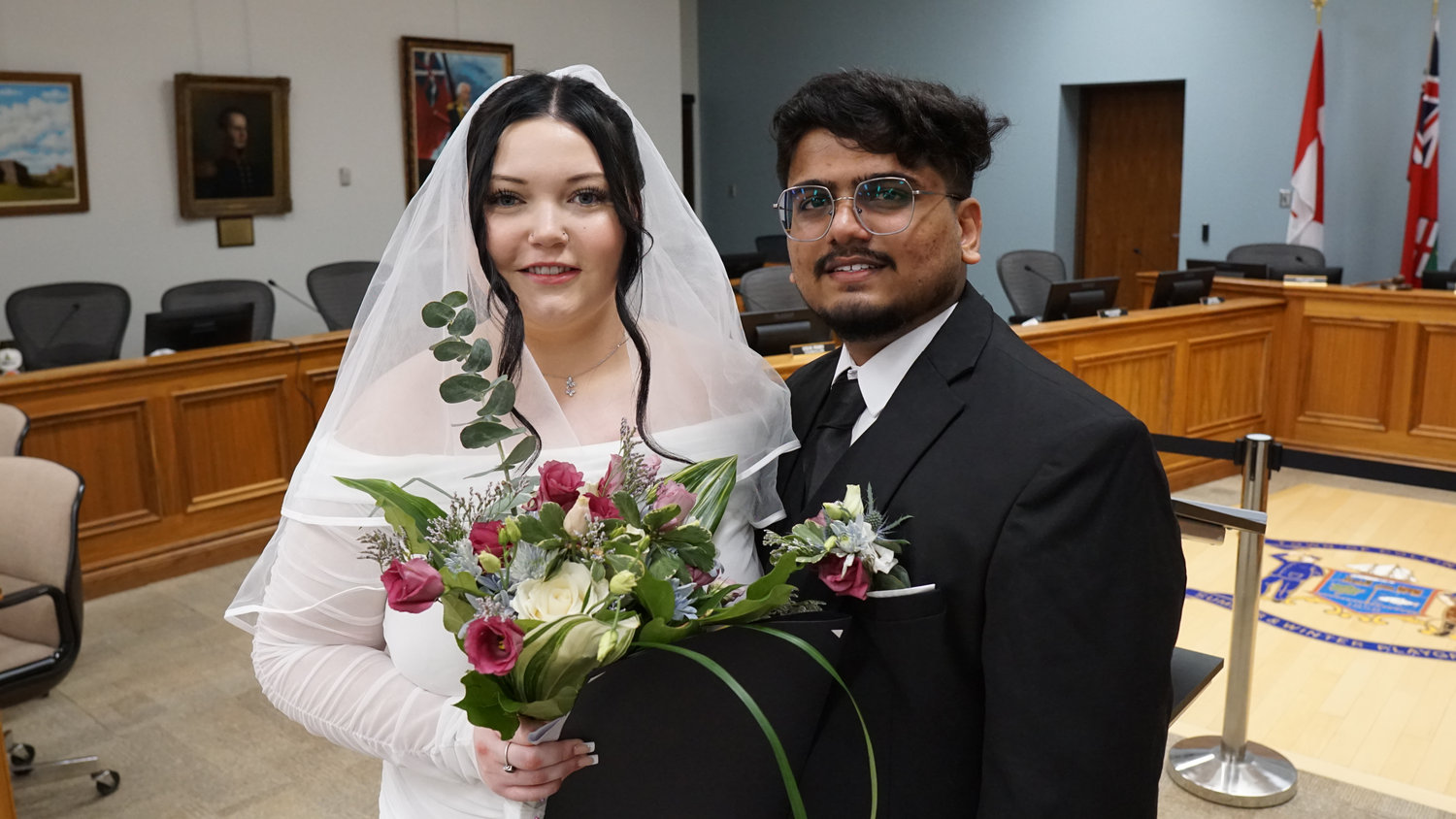Bride and groom posing in a ceremony room with flags in the background